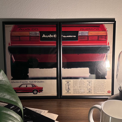 Gerahmte Oldtimer-Werbung des Audi 80 Quattro, stilvoll auf einem Tisch präsentiert, umgeben von Vintage-Magazinen und einer Tasse. Perfektes Ambiente, das die klassische Eleganz des Posters zur Geltung bringt.