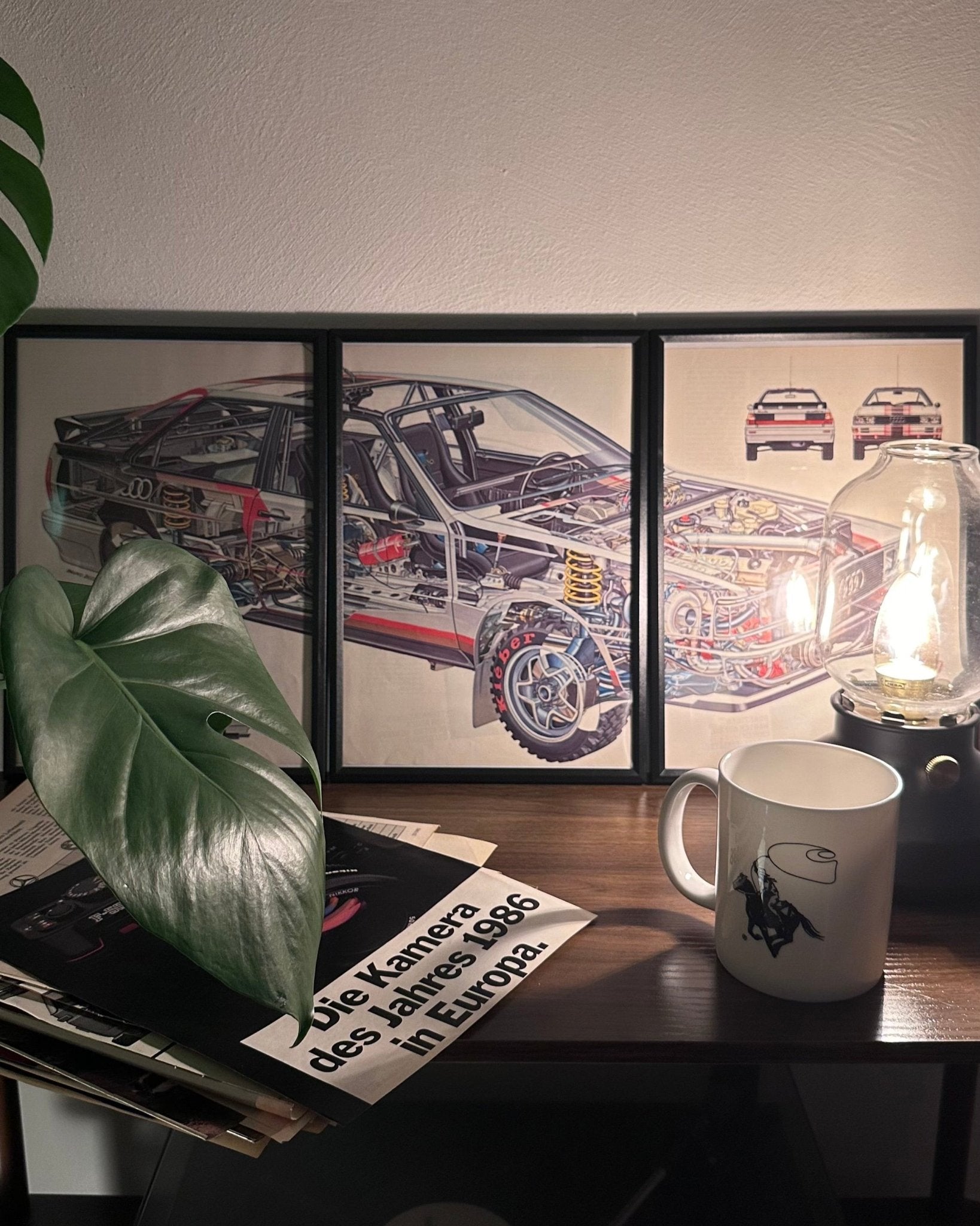 Gerahmte Oldtimer-Werbung des Audi Coupé Quattro, stilvoll auf einem Tisch präsentiert, umgeben von Vintage-Magazinen und einer Tasse. Perfektes Ambiente, das die klassische Eleganz des Posters zur Geltung bringt.