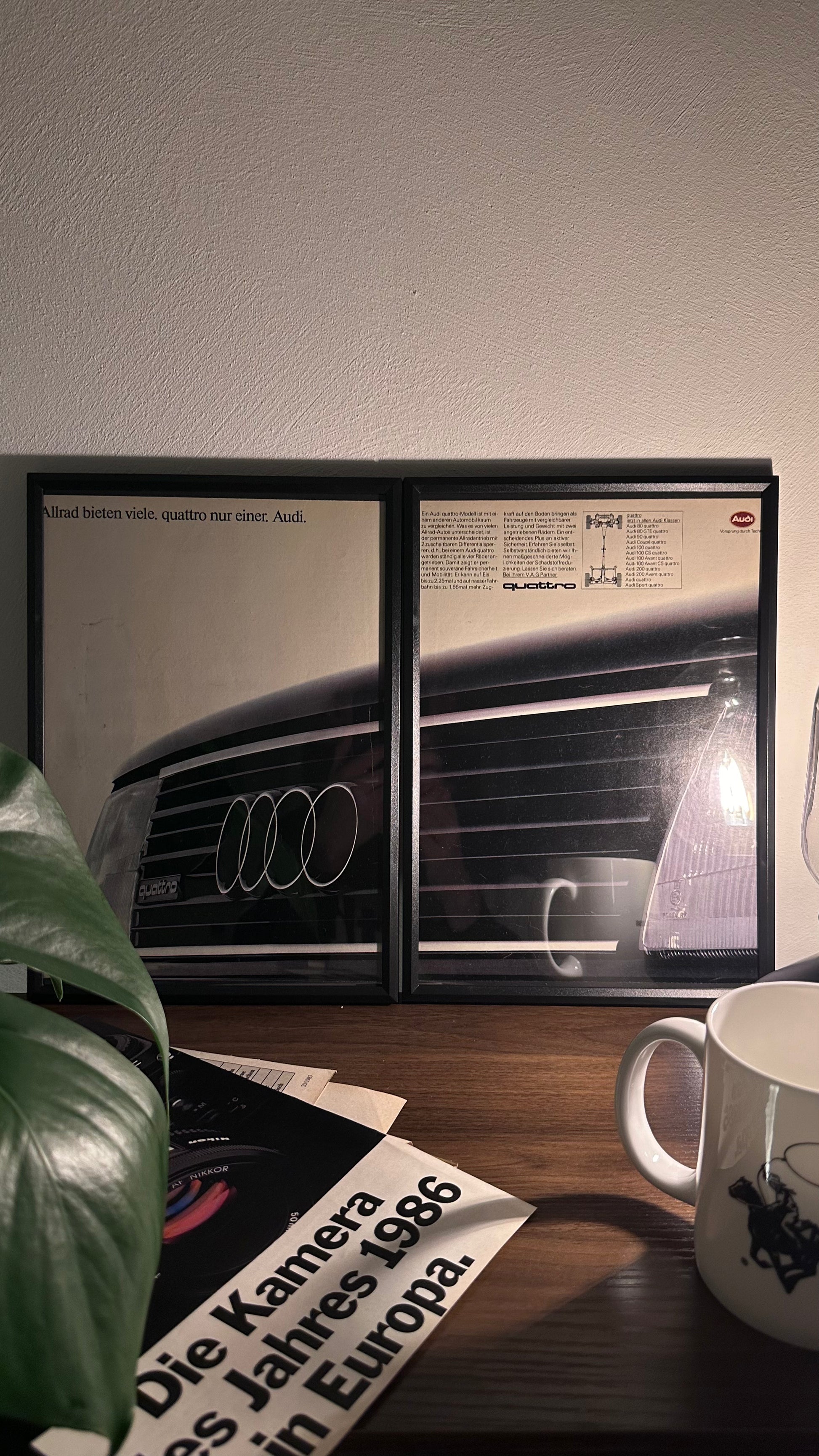 Gerahmte Oldtimer-Werbung des Audi Quattro aus den 80er Jahren, stilvoll auf einem Tisch präsentiert, umgeben von Vintage-Magazinen und einer Tasse. Perfektes Ambiente, das die klassische Eleganz des Posters zur Geltung bringt.