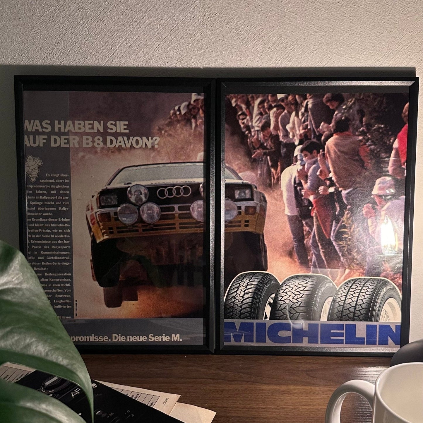 Gerahmte Oldtimer-Werbung des Audi Quattro, stilvoll auf einem Tisch präsentiert, umgeben von Vintage-Magazinen und einer Tasse. Perfektes Ambiente, das die klassische Eleganz des Posters zur Geltung bringt