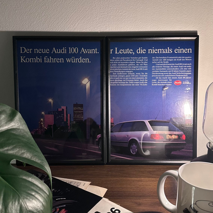 Gerahmte Oldtimer-Werbung des Mercedes-Benz W123 auf einem Tisch platziert, umgeben von Vintage-Magazinen und einer Tasse. Schlichtes und stilvolles Dekor, das den klassischen Charakter des gerahmten Posters unterstreicht."