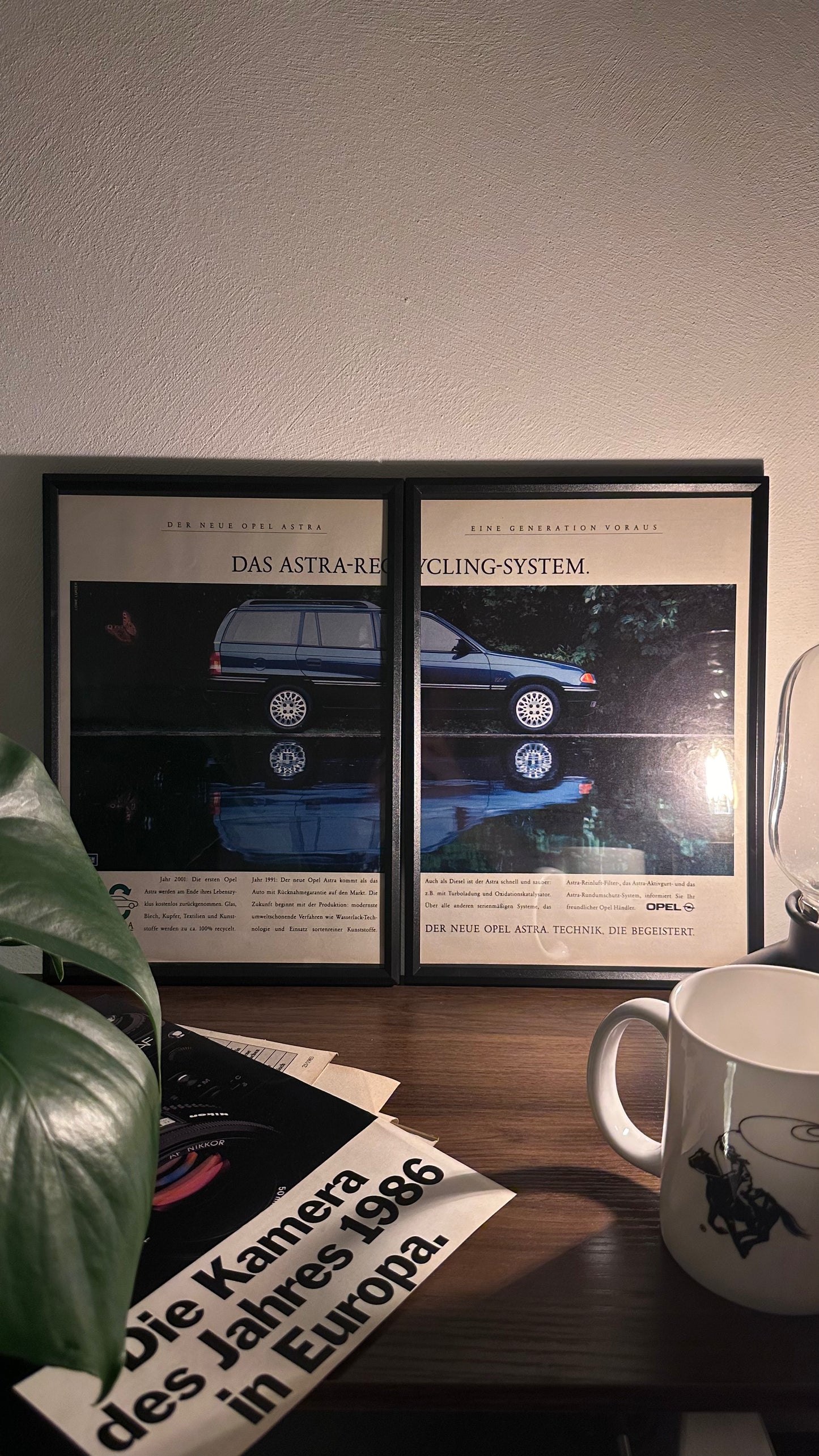 Gerahmte Oldtimer-Werbung des Opel Astra, stilvoll auf einem Tisch präsentiert, umgeben von Vintage-Magazinen und einer Tasse. Perfektes Ambiente, das die klassische Eleganz des Kompaktwagens zur Geltung bringt.