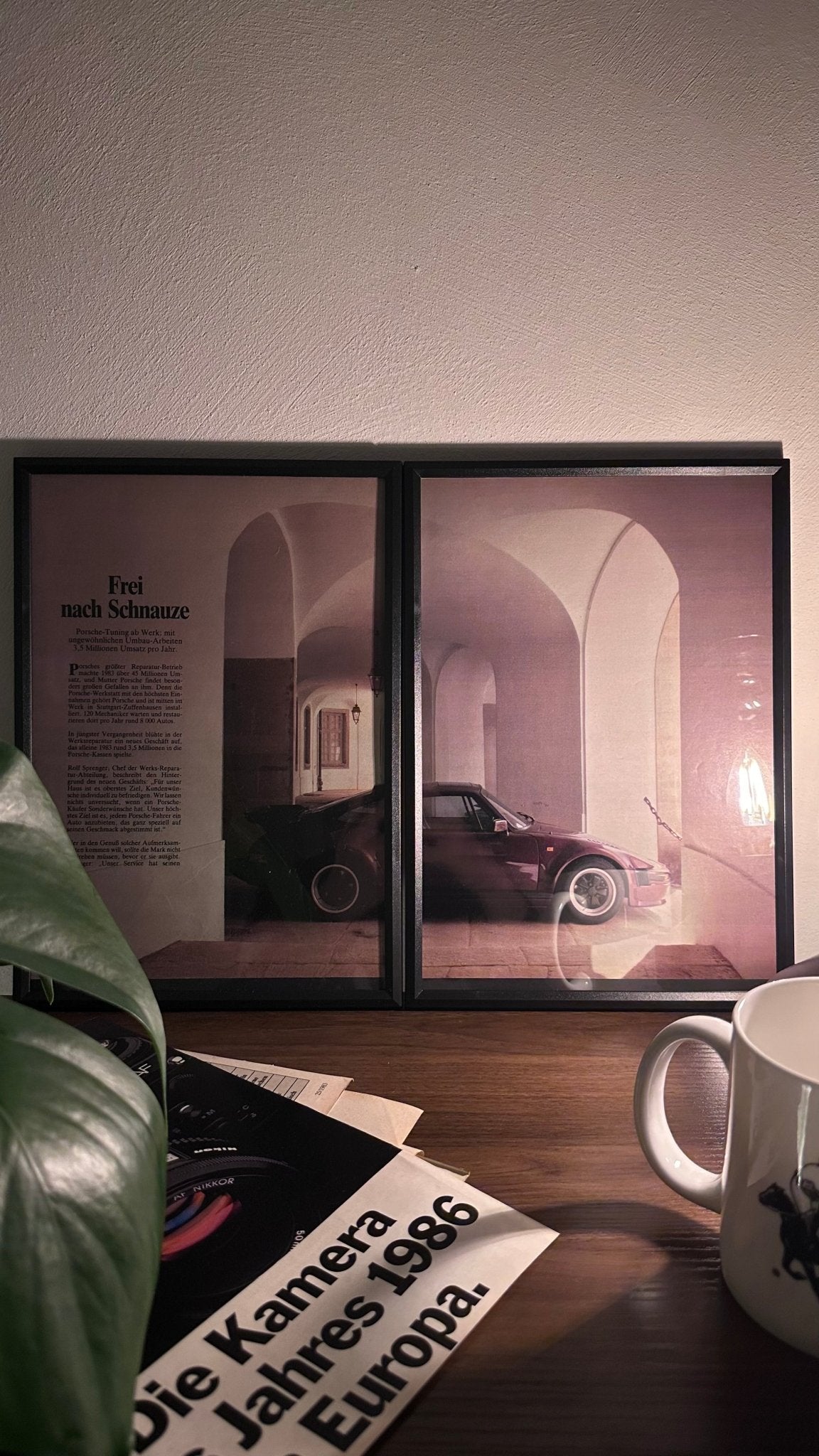 Gerahmte Oldtimer-Werbung des Porsche 911 Turbo, stilvoll auf einem Tisch präsentiert, umgeben von Vintage-Magazinen und einer Tasse. Perfektes Ambiente, das die ikonische Sportlichkeit des Porsche-Klassikers zur Geltung bringt