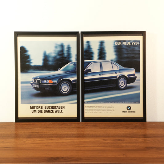 Original vintage BMW 7 Series advertisement framed in black aluminum. Two-piece wall art set showing a dark blue BMW 728i in motion with the German slogan 'Mit drei Buchstaben um die ganze Welt'.
