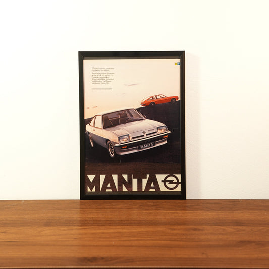 Original vintage Opel Manta advertisement framed in black aluminum. Single wall art piece showing a silver Manta coupe in the foreground and an orange model in the background with large MANTA text and Opel logo.